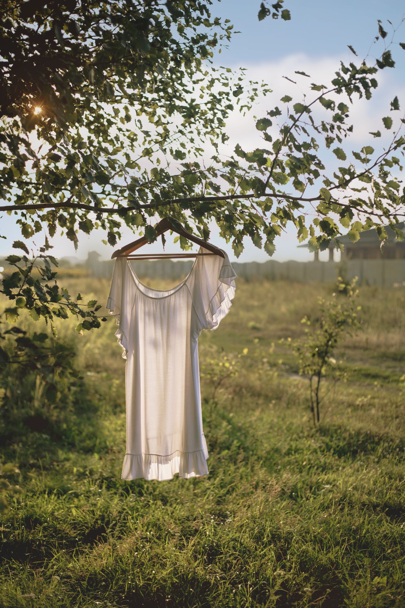 A pale dress on a wooden hanger, caught in low evening light